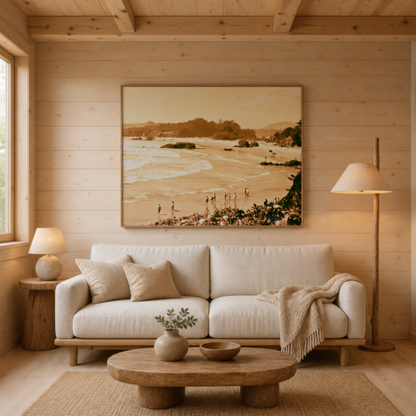 Coastal cove in sepia above a cream sofa on a pale pine plank wall with a floor lamp