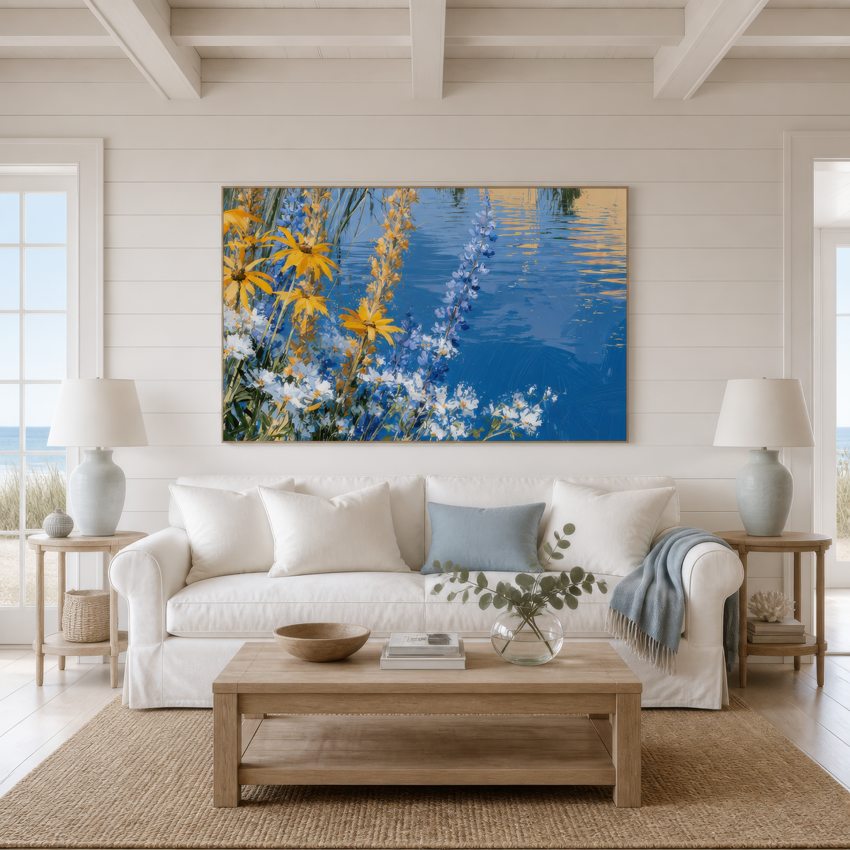 Wildflowers by the water above a white slipcovered sofa with blue pillows and two table lamps