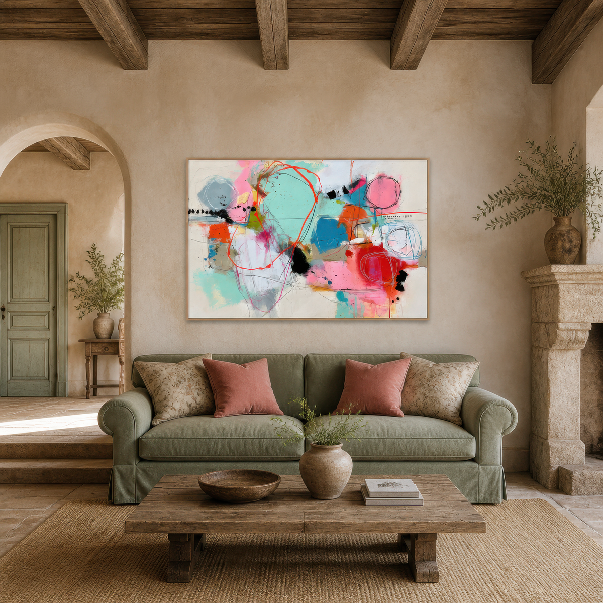 Pastel abstract collage above a sage green sofa with pink pillows and a wood table