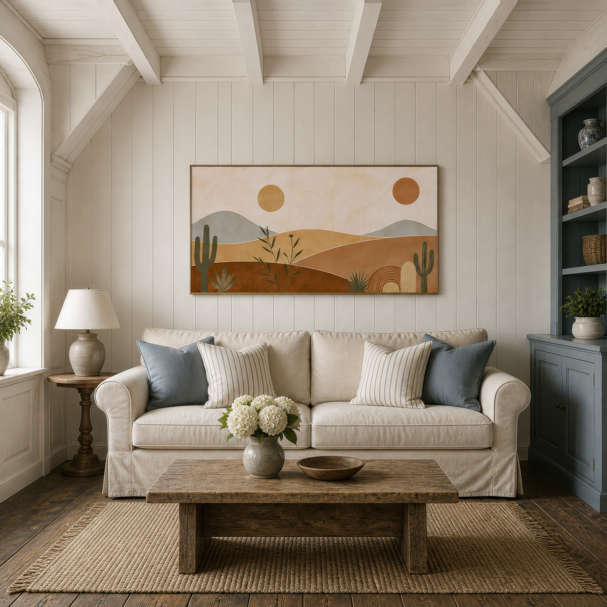 Desert dunes with cacti above a white slipcovered sofa with blue pillows and two lamps