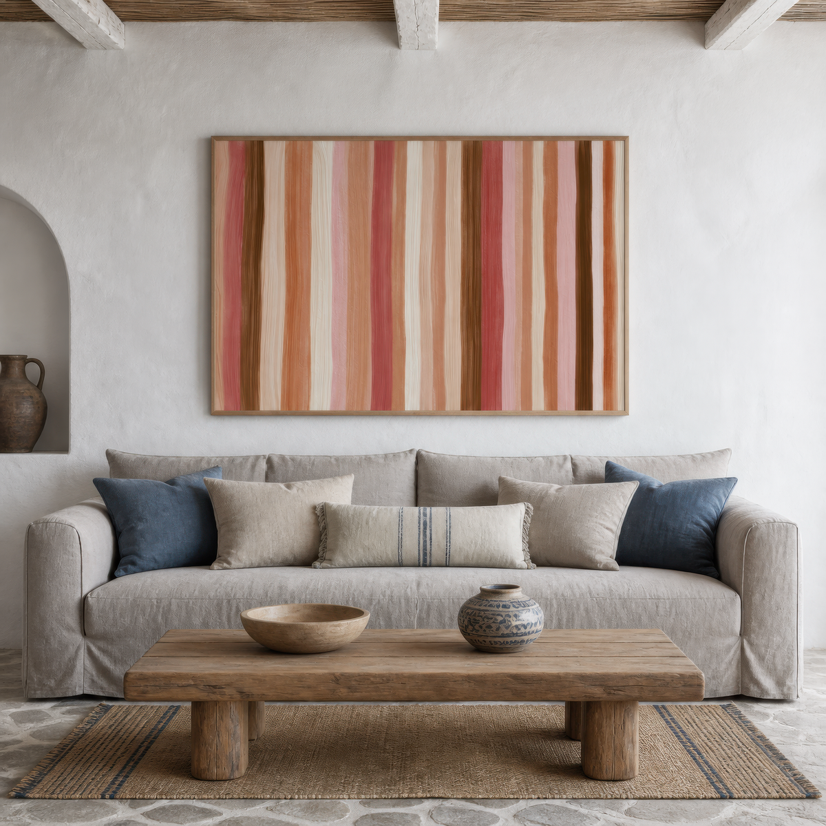 Terracotta and rose stripe artwork above a light grey sofa with navy pillows in a plaster room
